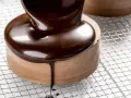 Un glaçage chocolat brillant et onctueux recouvre un petit gâteau rond, coulant sur les côtés.