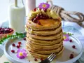 Pile de pancake banane avoine, garnie de fruits rouges, de rondelles de banane et de fleurs roses. Un délice matinal !