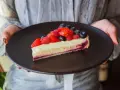 Tranche de tarte aux fruits rouges sur une crème mousseline onctueuse, présentée sur une assiette noire.