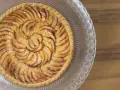 Un magnifique appareil tarte aux pommes, aux pommes caramélisées disposées en spirale sur une pâte dorée, sur un plat en verre décoré.