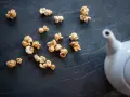 Pop corn caramel éparpillé sur une surface sombre, avec une théière blanche en arrière-plan.