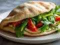 Sandwich pita garni de houmous, roquette et tomates. Une recette simple et savoureuse.