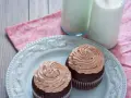 Deux cupcakes au chocolat avec une ganache chocolat passion onctueuse, servis sur une assiette bleue avec deux verres de lait.