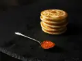 Une cuillère de caviar rouge sur une assiette noire, à côté d'une pile de blinis dorés. Parfait pour une recette blinis gourmande.