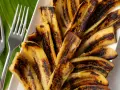 Bananes flambées grillées sur une feuille de bananier, prêtes à être dégustées avec deux fourchettes.