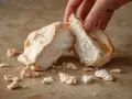 Une main casse une meringue aérienne, parfaite pour une recette meringue. Des miettes tombent sur le plan de travail.