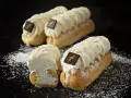 Trois éclairs chantilly généreusement garnis de crème fouettée, ornés d'un carré de chocolat, saupoudrés de sucre glace.