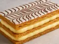 Une délicieuse feuille en pâtisserie, empilée avec de la crème pâtissière et décorée de glaçage blanc et chocolat.