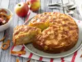Un délicieux gâteau aux pommes, doré et moelleux, avec des morceaux de fruits visibles. Des pommes fraîches et des chips de pommes complètent la scène.