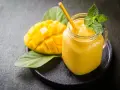 Un smoothie mangue onctueux dans un pot en verre, garni de menthe fraîche, à côté d'une moitié de mangue coupée en dés.