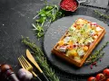 Gaufre salée garnie de fromage, de dés de mangue et de pousses, sur une ardoise noire.