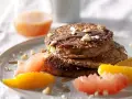 Pile de pancakes muesli, nappés de sirop et garnis de noix, accompagnés de quartiers d'agrumes.