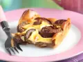 Tranche de clafoutis aux prunes moelleux sur une assiette rose avec une fourchette.
