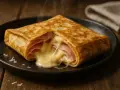 Crêpe garnie de jambon et de fromage fondant, dégageant une vapeur appétissante. Un délice simple et réconfortant.