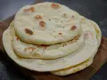 Pile de pains arabes moelleux, légèrement dorés par la cuisson, sur une planche en bois. Parfait pour accompagner un repas.