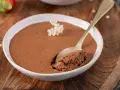 Une cuillère prend une bouchée d'une mousse au chocolat au lait aérienne, décorée de petites fleurs blanches.