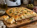 Une focaccia dorée, garnie de romarin frais et de gros sel, prête à être dégustée. Une recette simple pour un pain savoureux.