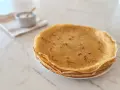 Pile de crêpes dorées, parfaites pour une recette crêpe moelleuse. Un petit bol de sucre est à côté.