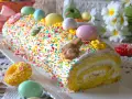 Bûche roulée décorée pour Pâques, recouverte d'un glaçage mascarpone facile et de vermicelles colorés, avec des œufs et un lapin en chocolat.