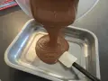 Une ganache au chocolat, inspirée par le Toblerone, est versée dans un plat métallique. Une spatule aide à l'étaler.