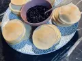 Une assiette bleue et blanche présente des piles de poffertjes dorés, accompagnés d'un bol de confiture de myrtilles. Parfait pour une recette de poffertjes !