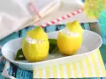 Deux citrons évidés remplis de sorbet citron, servis sur une assiette blanche, avec des feuilles vertes et des pailles colorées en arrière-plan.