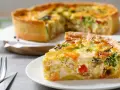 Une part de quiche savoureuse avec une pâte à tarte maison dorée, garnie de légumes et de poulet. Le reste de la tarte est flou en arrière-plan.