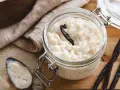 Un pot en verre rempli de riz au lait au four, garni d'une gousse de vanille. Une cuillère à côté en témoigne.