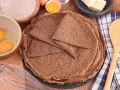 Pile de crêpes de sarrasin, avec des ingrédients pour la pâte à crêpe sarrasin : farine, œufs, beurre.
