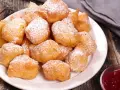 Une assiette de beignets banane saupoudrés de sucre glace, prêts à être dégustés avec une confiture de fruits rouges.
