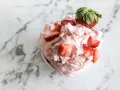 Un délice rose et crémeux : un sorbet fraise garni de morceaux de fruits frais et d'une fraise entière sur un fond marbré.