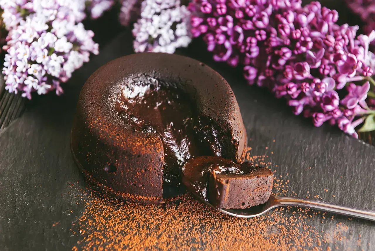 Un fondant au chocolat coulant, saupoudré de cacao, avec des fleurs de lilas en arrière-plan. Une bouchée parfaite.