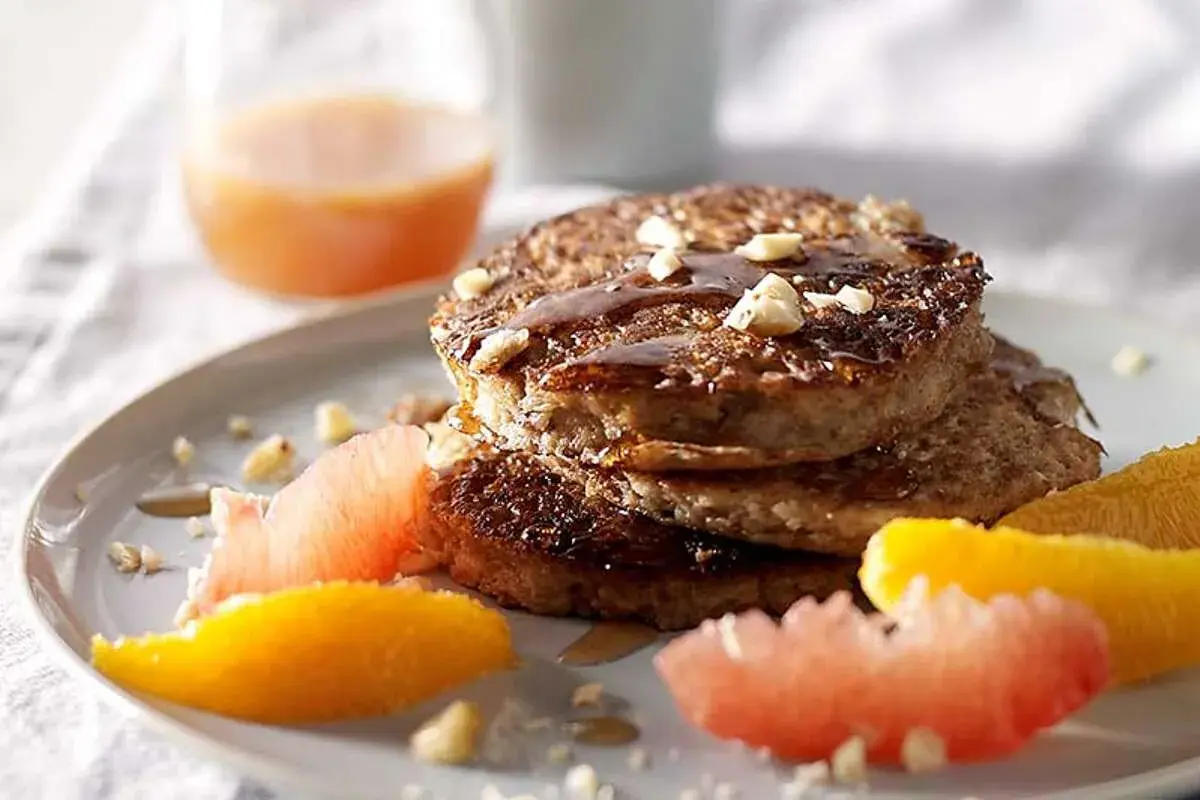 Pile de pancakes muesli, nappés de sirop et garnis de noix, accompagnés de quartiers d'agrumes.