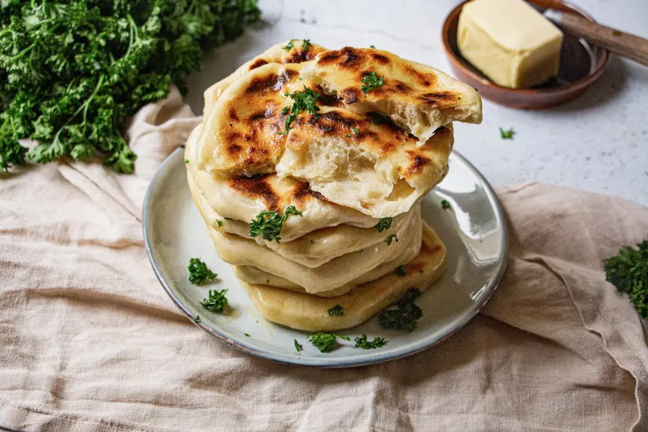 Pile de cheese naan moelleux, dorés et parsemés de persil frais. Un délice à déguster avec du beurre.