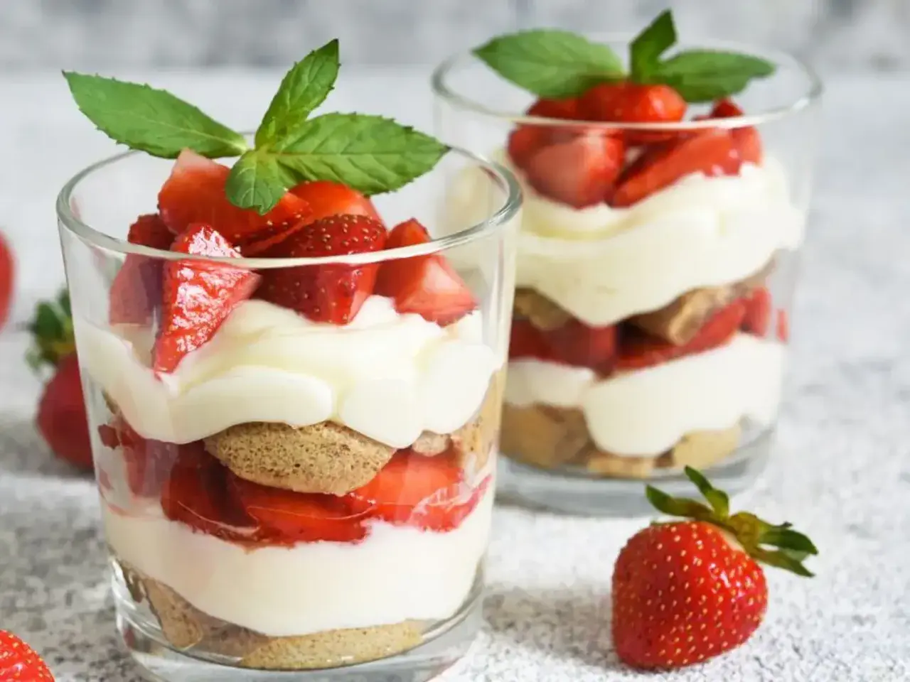 Deux verrines de tiramisu fraise, garnies de fruits rouges frais et de feuilles de menthe.