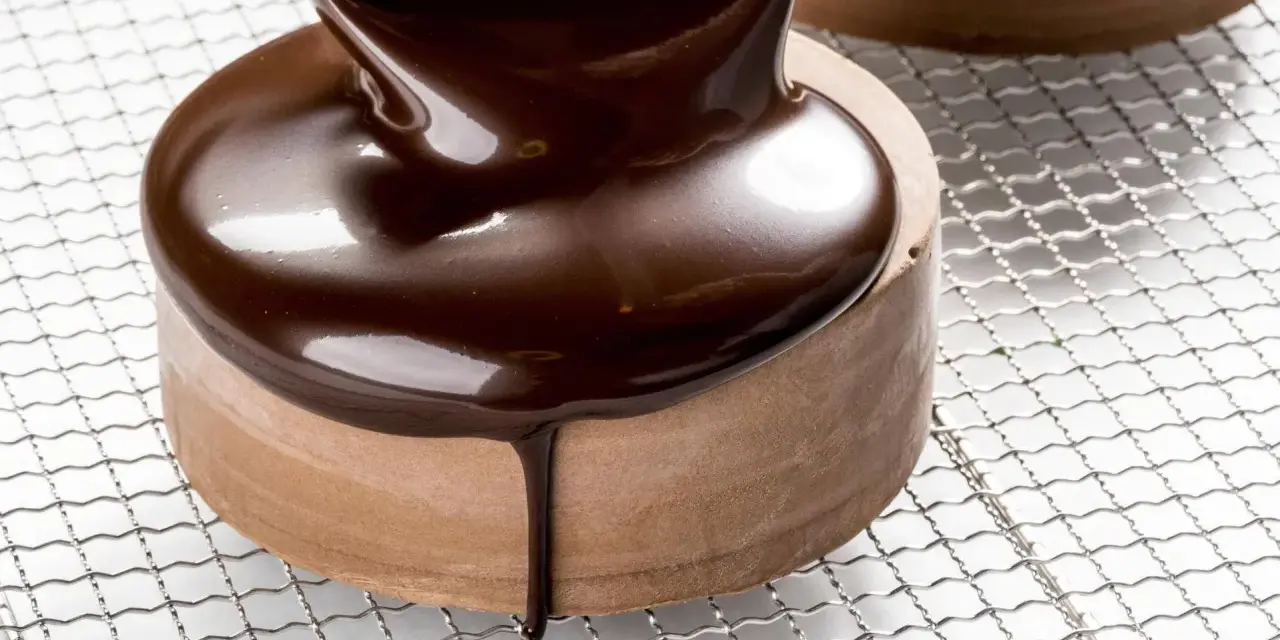 Un glaçage chocolat brillant et onctueux recouvre un petit gâteau rond, coulant sur les côtés.