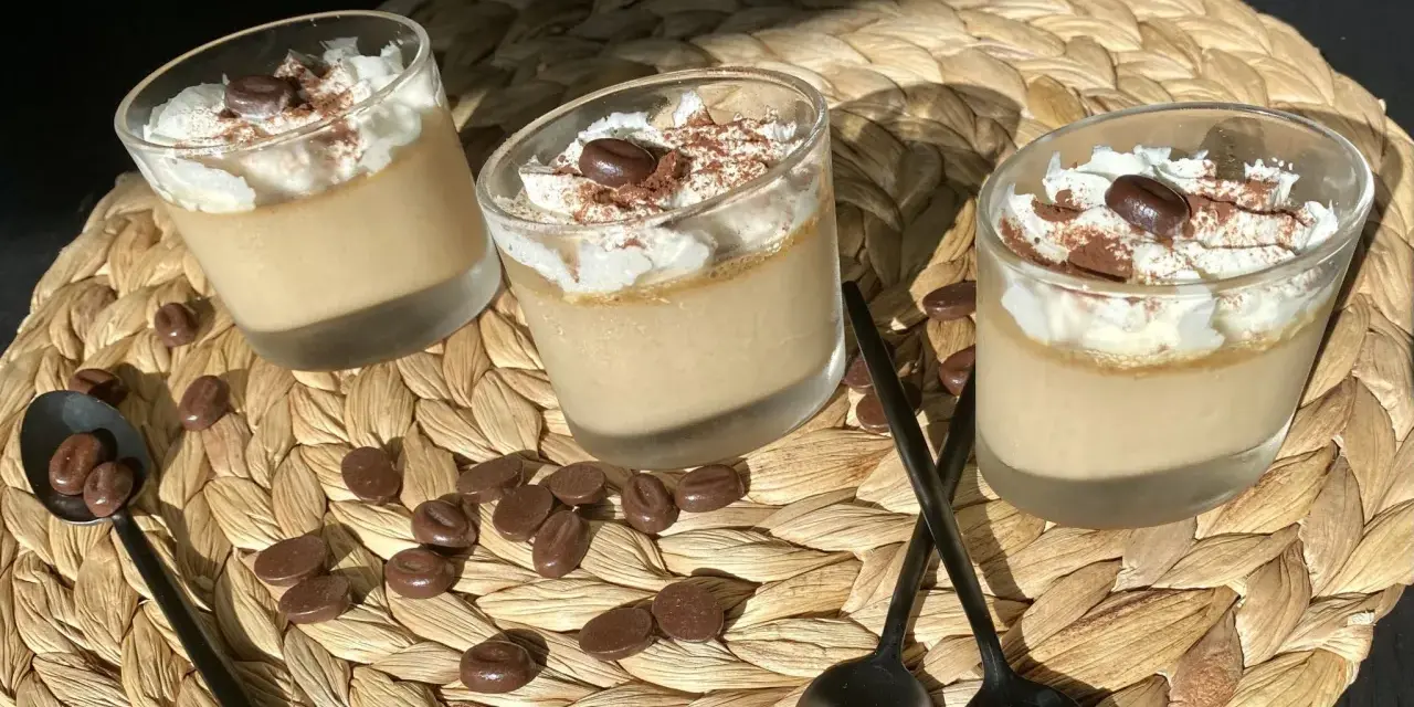 Trois verrines de crème au café facile, garnies de chantilly, cacao et grains de café. Des chocolats en forme de grains parsèment le napperon.