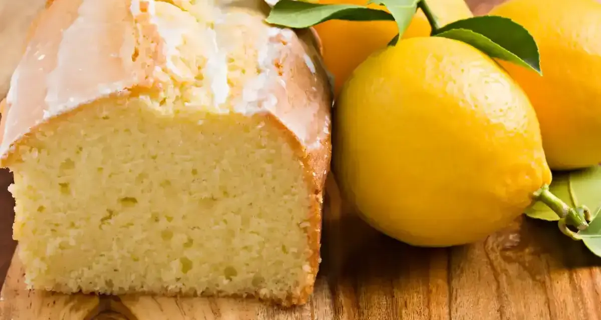 Un délicieux gâteau citron, avec un glaçage blanc et des citrons frais sur une planche en bois.