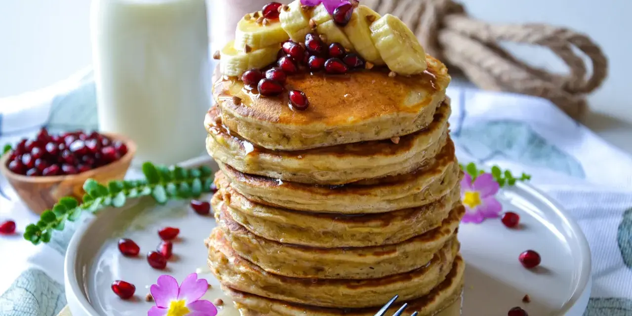 Pile de pancake banane avoine, garnie de fruits rouges, de rondelles de banane et de fleurs roses. Un délice matinal !