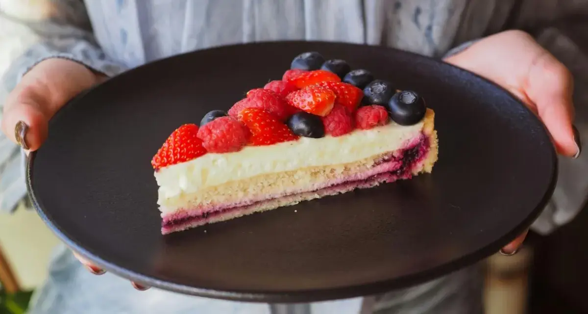 Tranche de tarte aux fruits rouges sur une crème mousseline onctueuse, présentée sur une assiette noire.