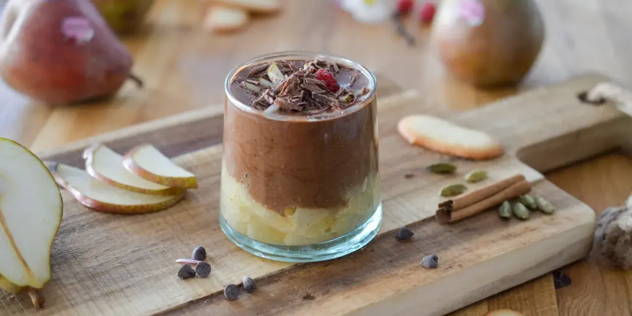 Délicieuse recette mousse poire chocolat, garnie de copeaux de chocolat et d'une framboise. Poires fraîches et épices sur fond de bois.