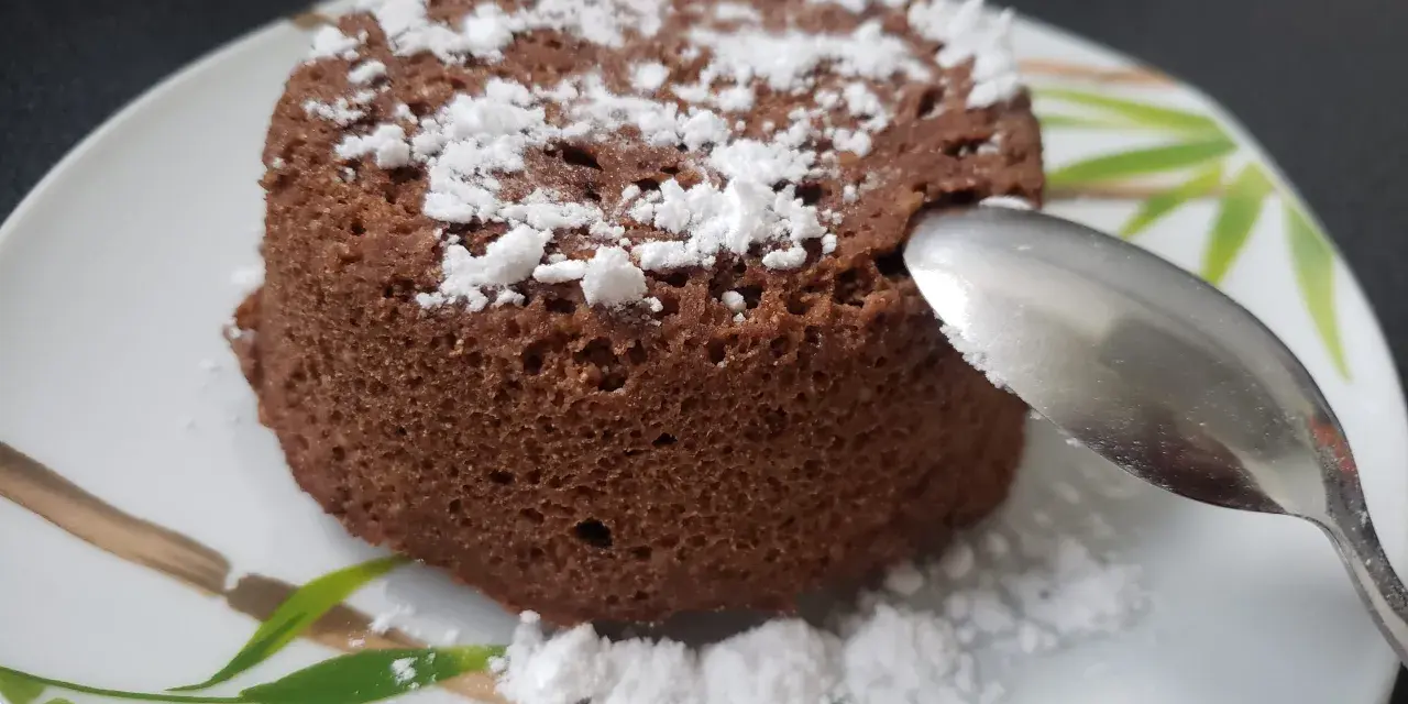 Un délicieux bowl cake au chocolat, saupoudré de sucre glace, prêt à être dégusté avec une cuillère.