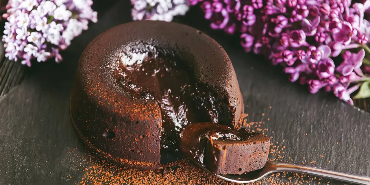 Un fondant au chocolat coulant, saupoudré de cacao, avec des fleurs de lilas en arrière-plan. Une bouchée parfaite.