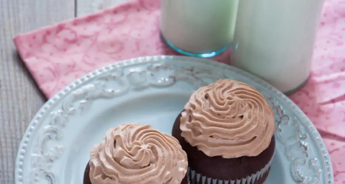 Deux cupcakes au chocolat avec une ganache chocolat passion onctueuse, servis sur une assiette bleue avec deux verres de lait.