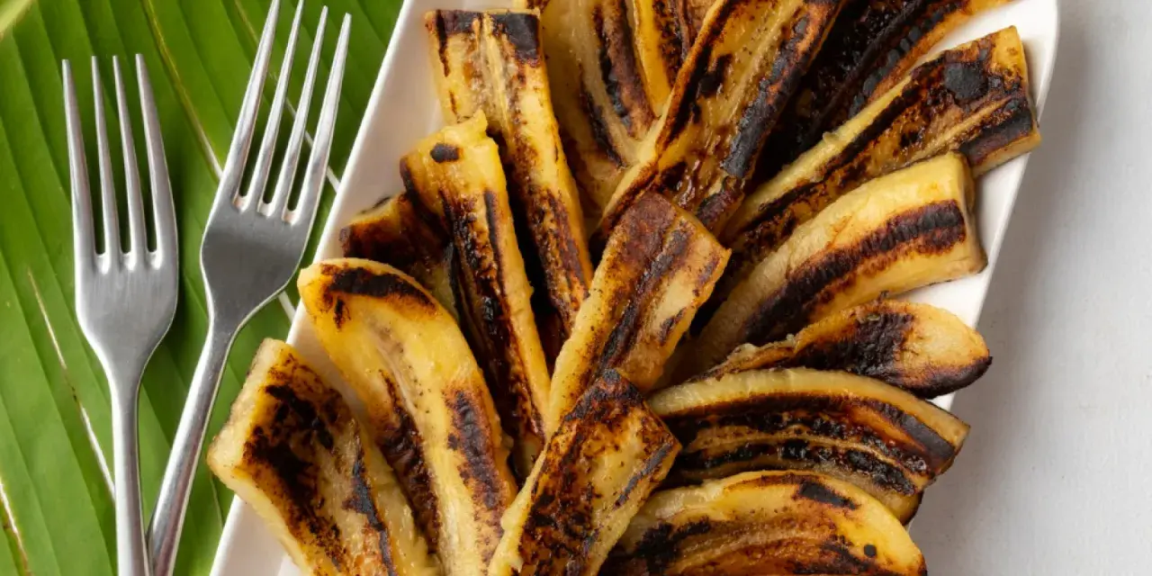Bananes flambées grillées sur une feuille de bananier, prêtes à être dégustées avec deux fourchettes.