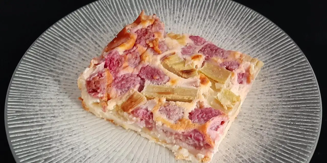 Tranche de clafoutis rhubarbe aux fruits rouges, sur une assiette transparente aux motifs rayonnants.