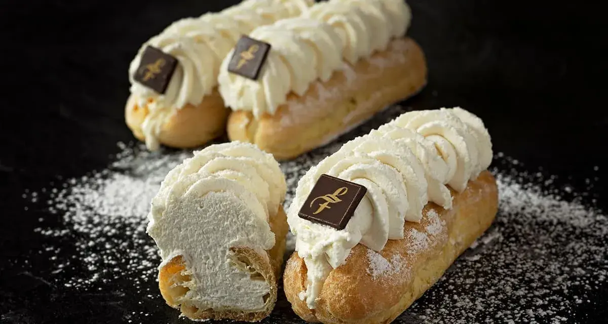 Trois éclairs chantilly généreusement garnis de crème fouettée, ornés d'un carré de chocolat, saupoudrés de sucre glace.