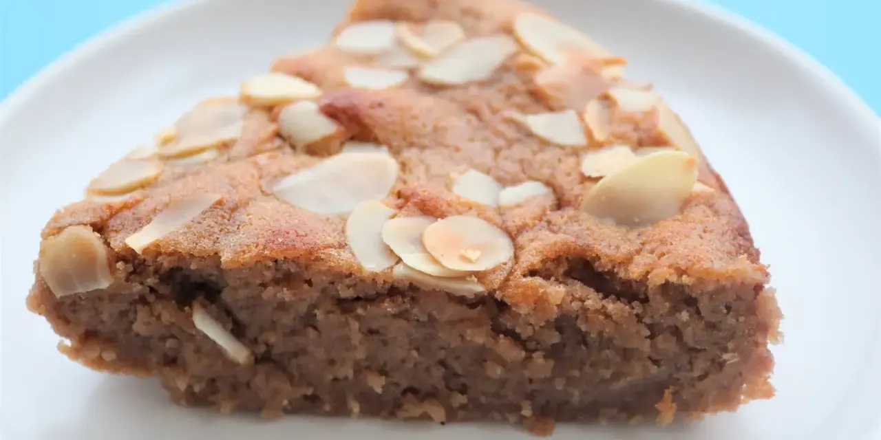 Tranche de gâteau à la crème de marron, garnie d'amandes effilées, sur une assiette blanche.