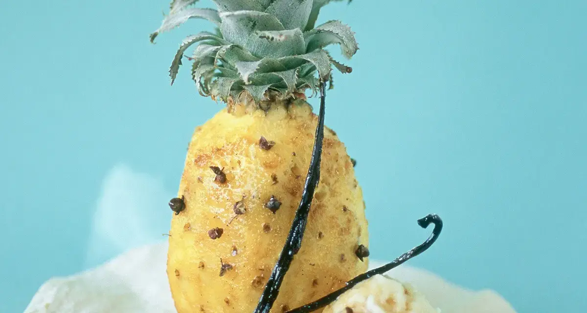 Un ananas rôti, parsemé de clous de girofle et de gousses de vanille, sur un fond bleu pâle. Un délice sucré et épicé.