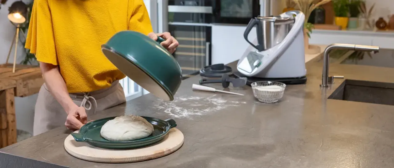 Préparation de la pâte à pizza avec un robot culinaire. Une boule de pâte repose sur un plat vert, prête à être cuite.